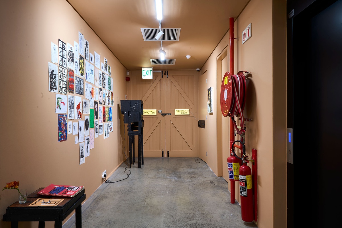 Installation photograph from Phillip Newman's exhibition in A4 Arts Foundation's Goods space. On the left, drawings are arranged on the wall. At the back, a screen is mounted in a wooden stand. On the right, a painting is mounted on the wall.
