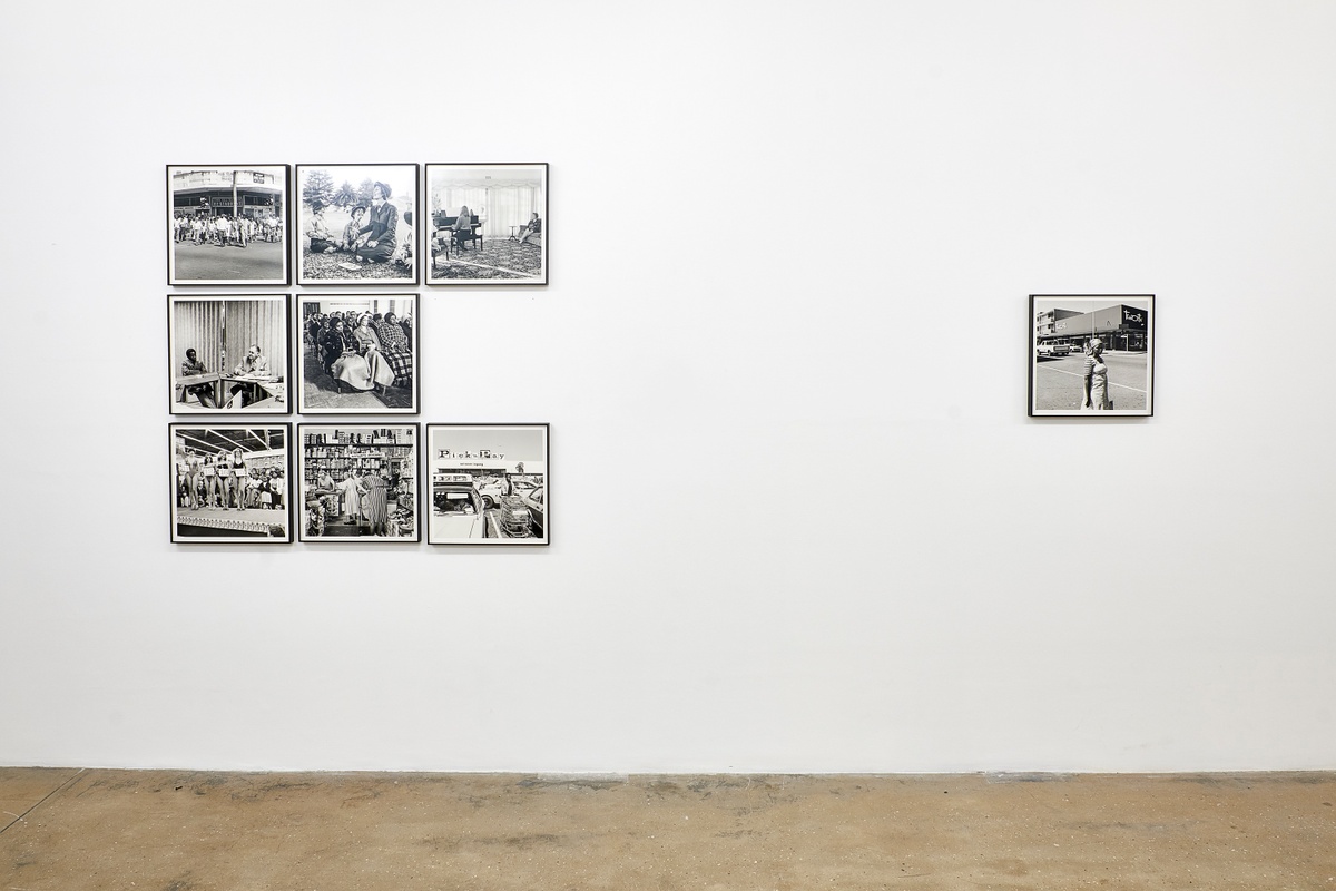 Installation photograph from the ‘Picture Theory’ exhibition in A4’s Gallery. On the left, eight monochrome photographs from David Goldblatt’s ‘In Boksburg’ series are mounted on the gallery wall in a 3 by 3 grid. On the right, Goldblatt’s monochrome photograph ‘On the corner of Commissioner and Eloff Streets’ is mounted on the gallery wall.
