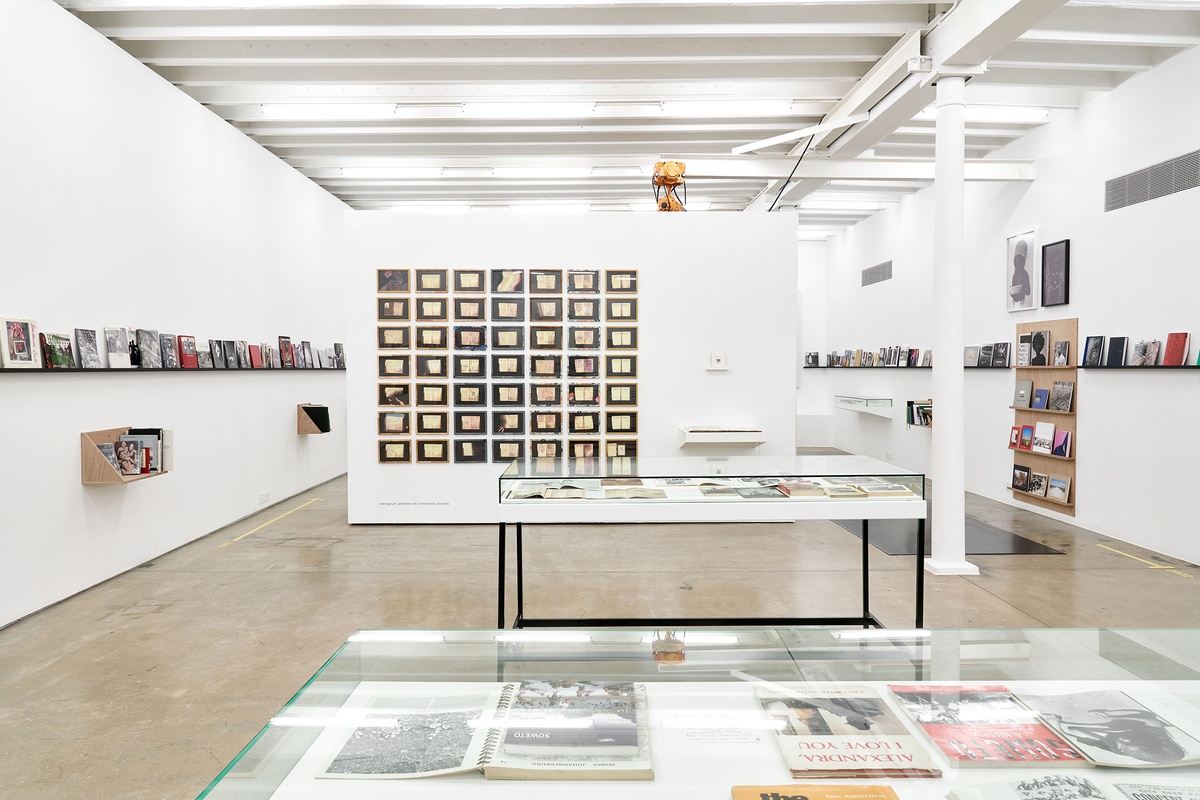 Installation photograph from the Photo Book! Photo-Book! Photobook! exhibition in A4’s Gallery. In the middle, Sue Williamson’s photographic series ‘For Thirty Years Next to His Heart’ hangs on a moveable wall in an area dedicated to photobooks from the years 1967 to 1994.
