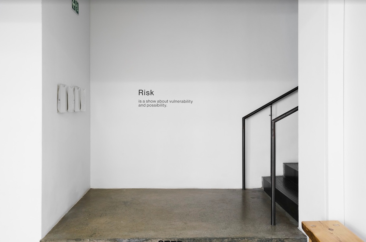 Installation photograph from the ‘Risk’ exhibition in A4’s Gallery. On the left, Pieter Hugo’s photographic series ‘The Journey’. At the back, the exhibition text reads ‘Risk is a show about vulnerability and possibility.’ On the right, a staircase leads up to the gallery.
