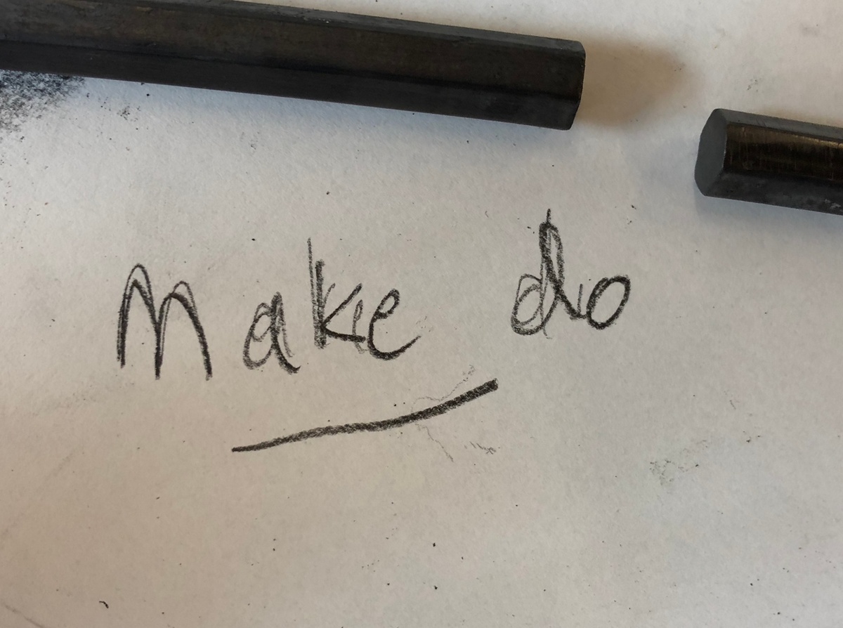 Process photograph from the More For Less exhibition in A4’s Gallery that shows a close-up view of the phrase ‘Make do’ written in charcoal on paper.
