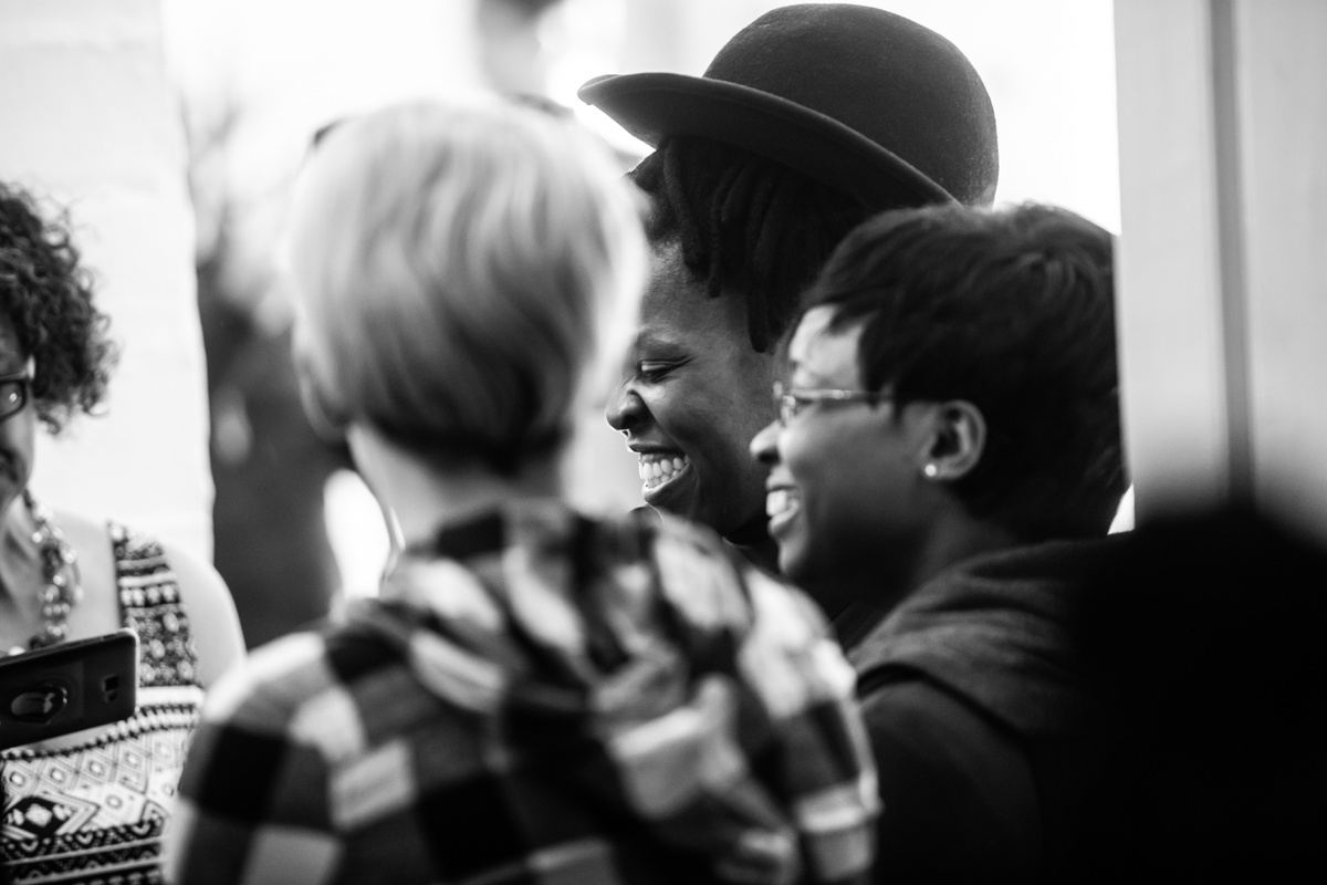 Monochrome event photograph from the opening of the “Ikhono LaseNatali” exhibition in A4’s Gallery that depicts a closeup view of Zanele Muholi with attendees.
