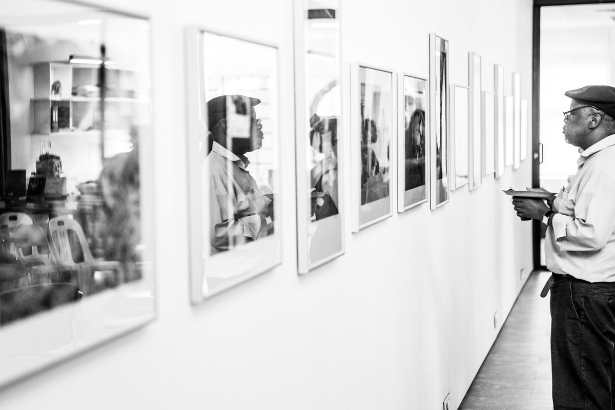 Monochrome event photograph from the launch of Omar Badsha’s book ‘Seedtimes’ on A4’s top floor. On the left, a row of Omar Badsha’s monochrome photographs are mounted on the wall. On the right, an attendee looks at the photographs.
