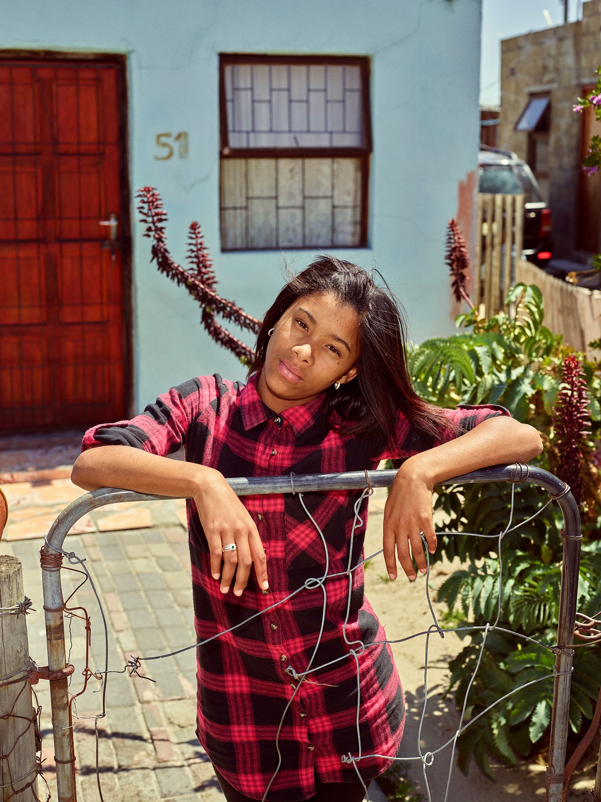 Photograph by Pieter Hugo, from A4’s ‘Atlantis Project’ exchange with the SWAGG United Dance Crew, that depicts a young person leaning on a metal gate in front of a house.
