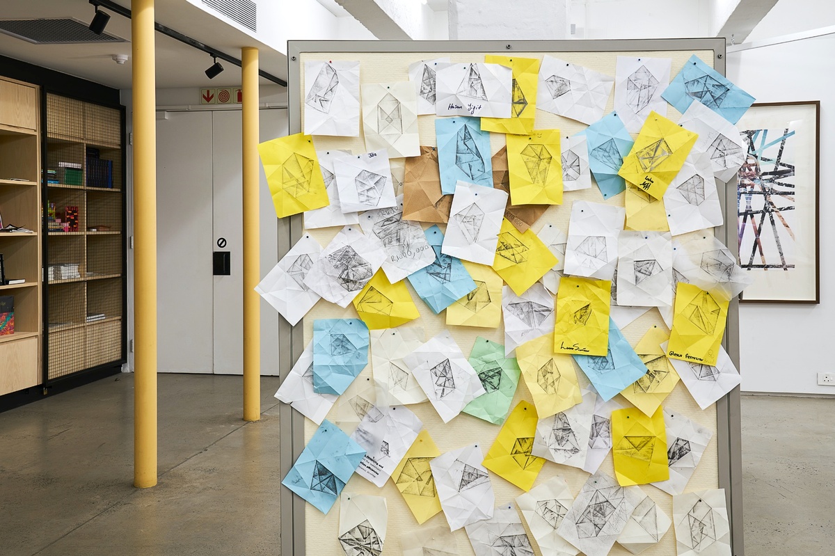 Process photograph from Christian Nerf’s participatory artwork ‘Teaching Teachers’ on A4’s ground floor. A white pinboard in A4’s library features multiple overlapping and multicoloured pages with graphite drawings and visible traces of having been folded.
