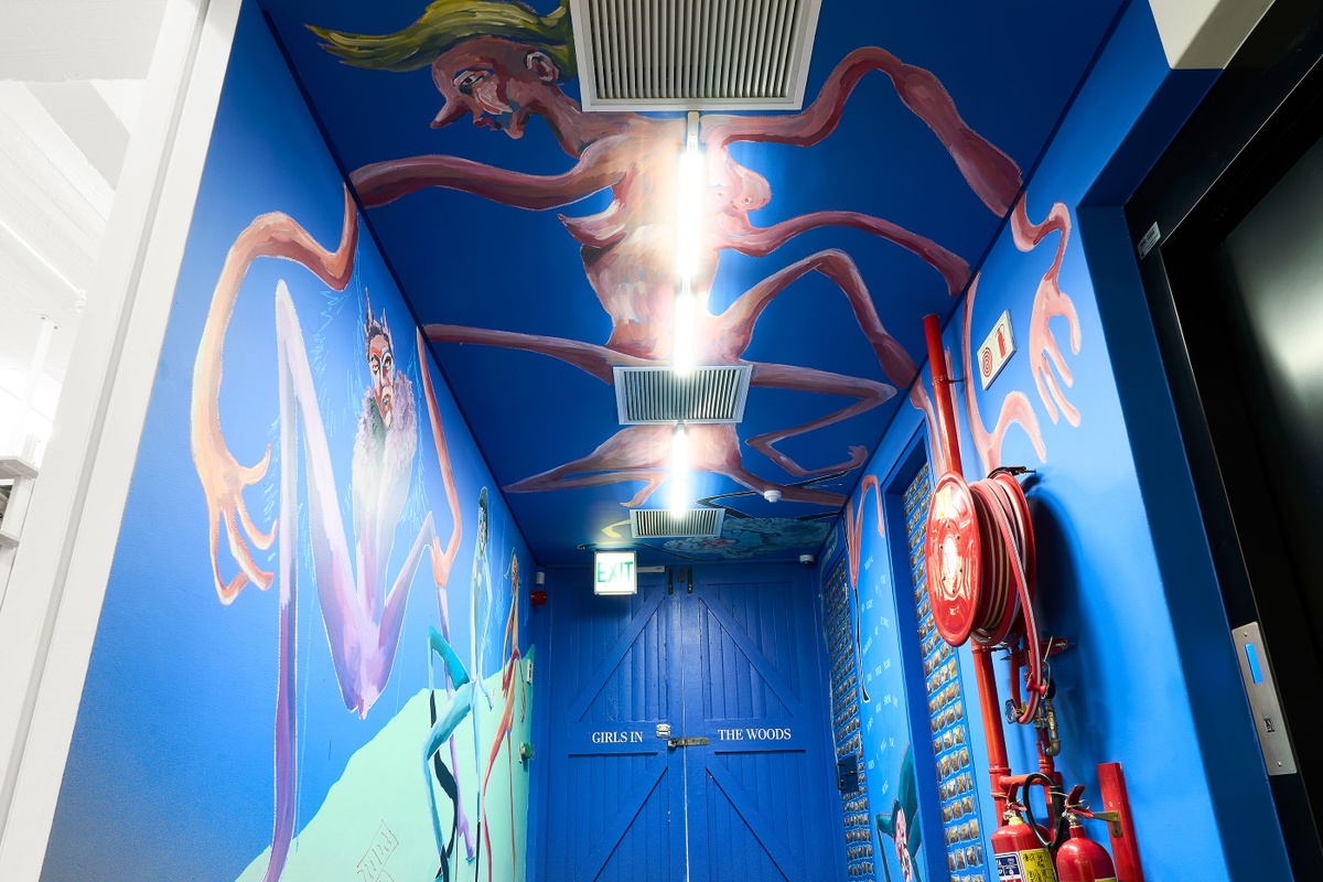 Installation photograph of Dominique Cheminais’ residency in A4’s Goods project space. A painted mural with humanoid figures lines the blue walls and ceiling.
