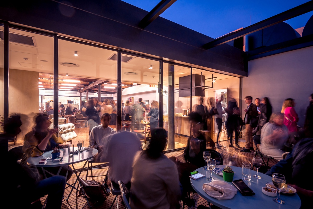 Event photograph from the opening of the You & I exhibition in A4’s Gallery that shows attendees seated and standing on A4’s top-floor deck.
