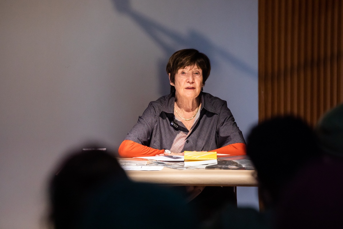 Event photograph from the book launch of 'ArtThrob: 25 Years of Art Writing in South Africa' in A4 Arts Foundation that shows artist Sue Williamson seated at the speakers' table, addressing the attendees.
