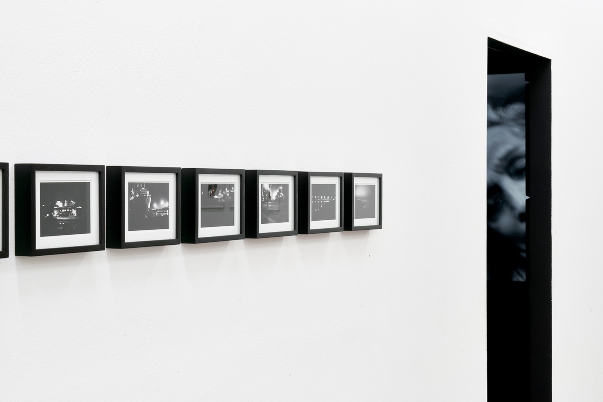 Installation photograph of the You to Me, Me to You exhibition. On the left, Bas Jan Ader’s 26 framed monochrome photographic prints ‘Study for In Search of the Miraculous (One Night in Los Angeles)’ are mounted on a white gallery wall in a straight line. On the right, Dayanita Singh’s projected video work ‘Mona and Myself’ is partially visible through the video room door.
