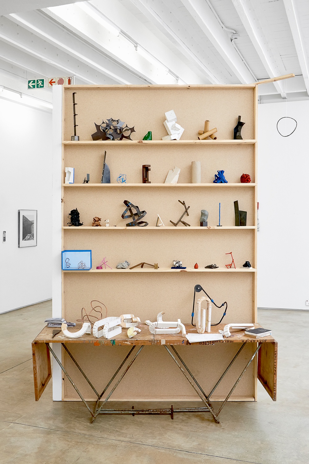 Installation photograph from the 2018 rendition of ‘Parallel Play’ in A4’s Gallery. At the back, Kyle Morland’s sculptural objects are arranged on a wooden shelving unit. At the front, Morland’s sculptural objects sit on a wooden table.
