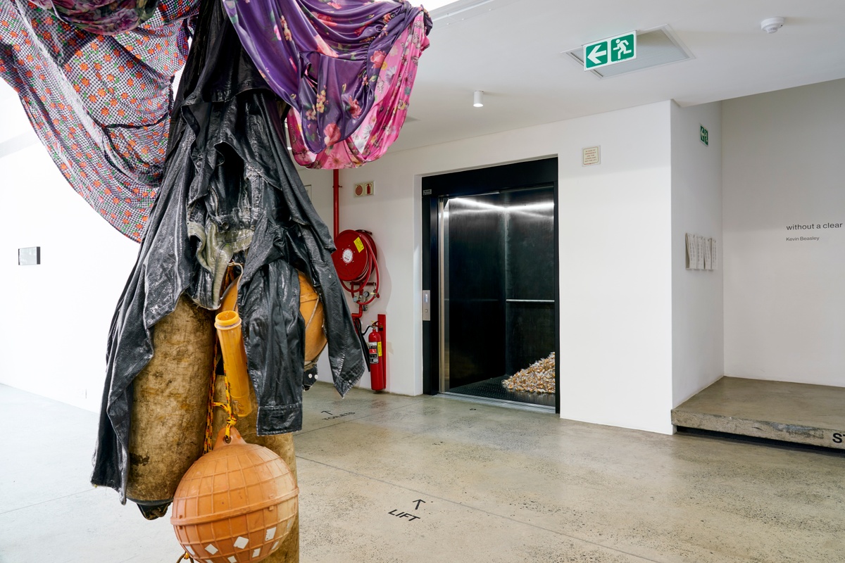 Installation photograph of Felix González-Torres' ‘Untitled (Fortune Cookie Corner)’ in A4’s elevator, with wrapped fortune cookies piled against the back of the interior. On the left, Kevin Beasley’s untitled sculptural work is suspended in A4’s foyer.
