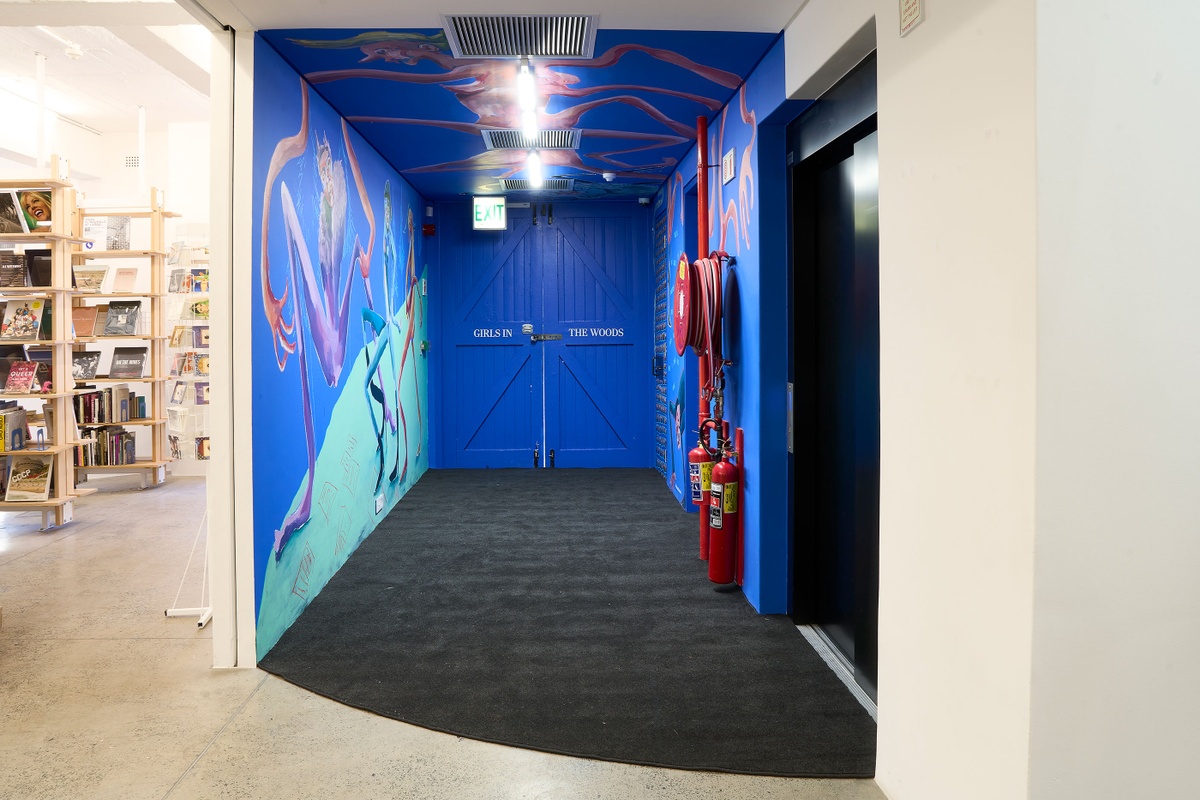 Installation photograph of Dominique Cheminais’ residency in A4’s Goods project space. A painted mural with humanoid figures lines the blue walls and ceiling.
