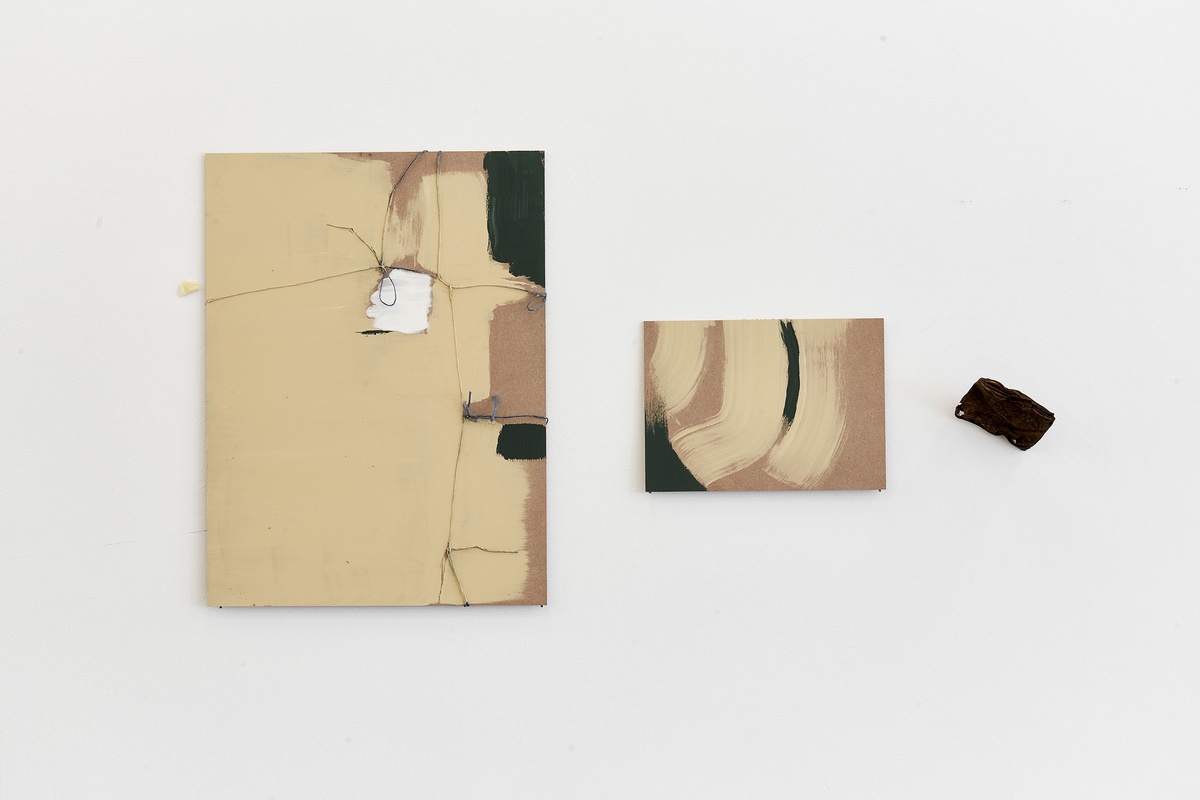 Process photograph from the 2nd rendition of ‘Parallel Play' in A4’s Gallery depicts work by Asemahle Ntlonti mounted on a white wall. On the left, a panel of processed wood with paint and thread. In the middle, a smaller panel of processed wood and paint. On the right, a small found object consisting of rusted metal.
