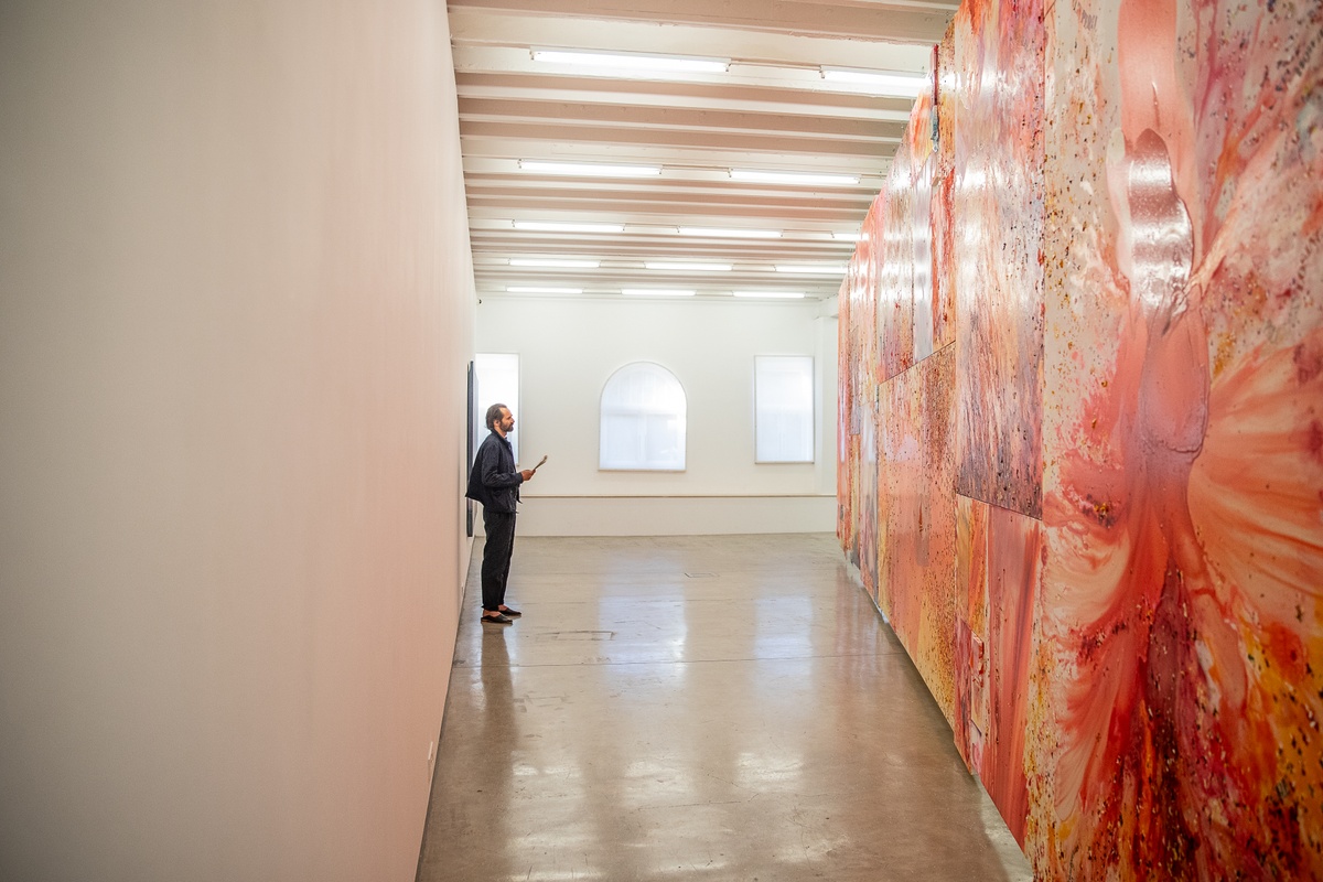 Event photograph from the preview of the 'A Little After This' exhibition in A4 Arts Foundation. On the right, an installation of Penny Siopis' glue, ink and oil 'Maitland' paintings is suspended from the ceiling. On the left, an attendee examines the installation.
