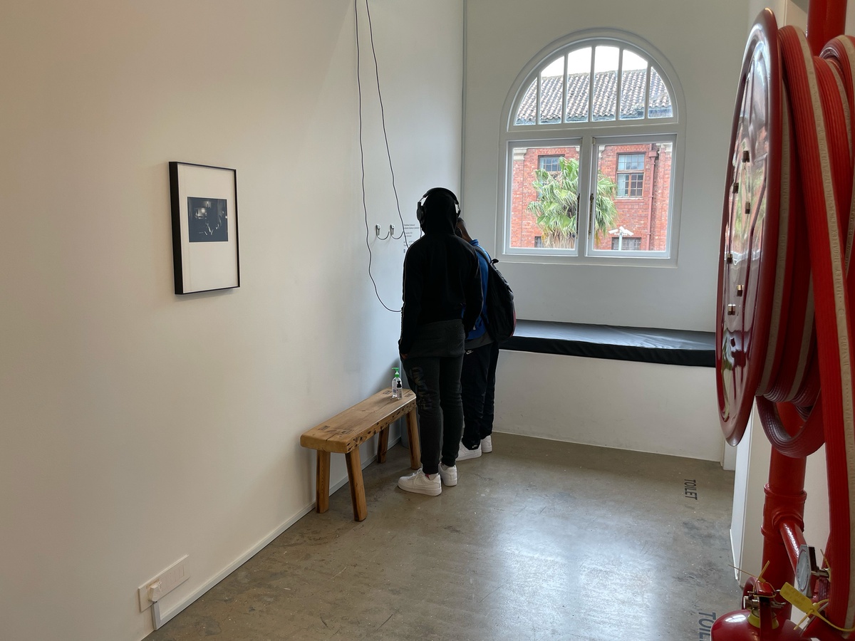Event photograph from the ‘Lalela x A4' exchange during the ‘Tell It to the Mountains’ exhibition in A4’s Gallery. On the left, Lidokuhle Sobekwa’s photograph ‘Death of George Floyd’. At the back, two students listening to a recording of Sobekwa in conversation with Thembinkosi Goniwe at a listening station with headphones.
