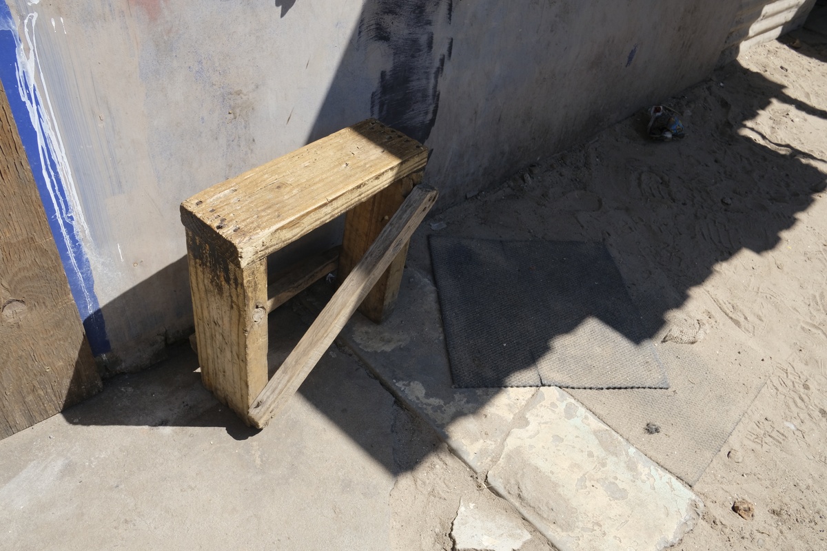 Process photograph from a visit to the Bonteheuwel township that formed part of ‘Open Production’, Igshaan Adams’ hybrid studio/exhibition in A4’s Gallery. A small wooden bench sits on concrete flooring that terminates in sand.
