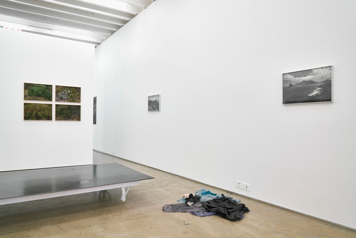 Installation photograph from the ‘without a clear discernible image’ exhibition in A4’s Gallery. At the front, Beasley’s untitled garment and resin work sits on the gallery floor next to a metal platform. On the right, Kevin Beasley’s monochrome photograph ‘Hout bay’ is mounted on the gallery wall. On the left, Beasley’s four-part photographic series ‘Luyolo’ is mounted on the gallery wall.
