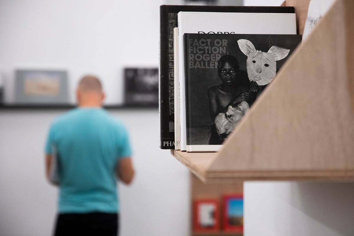 Event photograph from the opening of the Photo Book! Photo-Book! Photobook! exhibition in A4’s Gallery in an area used to house photobooks from the years 1994 to 2022. Roger Ballen’s photobook ‘Fact or Fiction’ sits on a wall-mounted wooden shelf.
