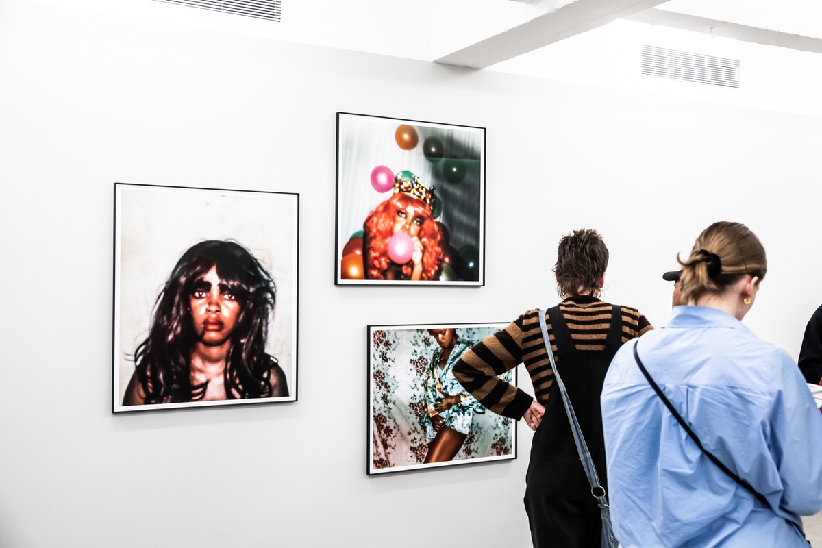 Event photograph from the opening of the ‘Model’ exhibition in A4’s Reading Room. Attendees stand in front of three framed photographs from Phumzile Khanyile’s ‘Plastic Crowns’ series.
