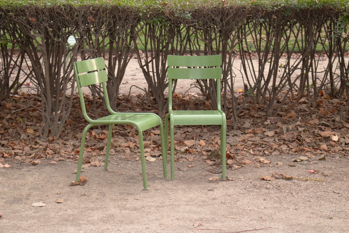 A photographic print from Thembinkosi Hlatshwayo’s ‘hearts can’t make it up’ series that depicts two green chairs arranged in front of a hedge.
