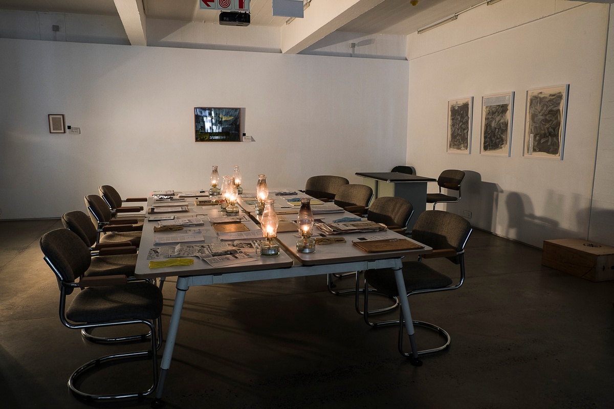 Installation photograph from the ‘Gladiolus’ exhibition on A4’s ground floor that depicts printed matter, oil lamps and archival gloves arranged on four tables.
