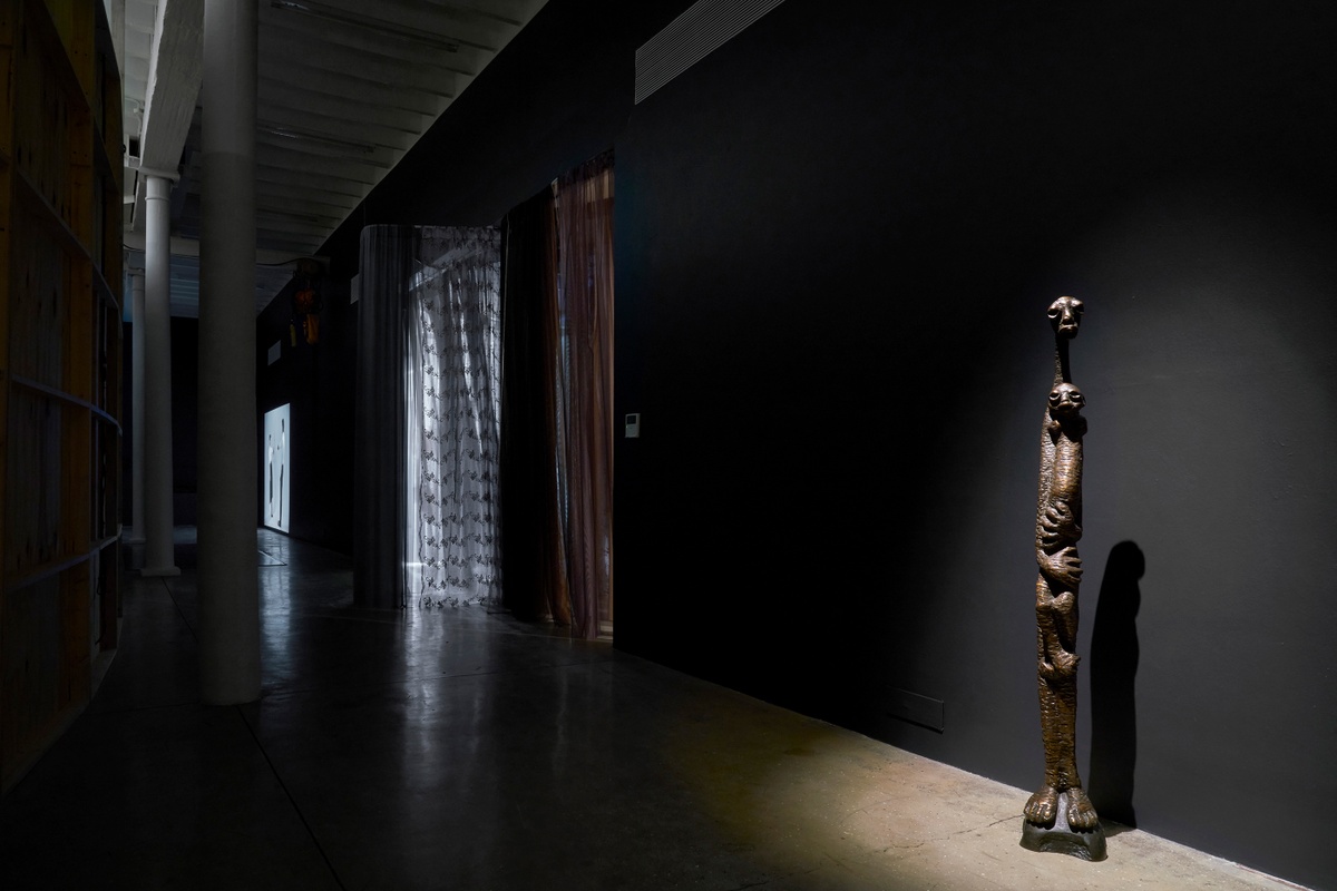 Installation photograph from the ‘Risk’ exhibition in A4’s Gallery. On the right, Lucas Sithole’s bronze sculpture ‘Mother and Child’ stand in front of the gallery wall. 
