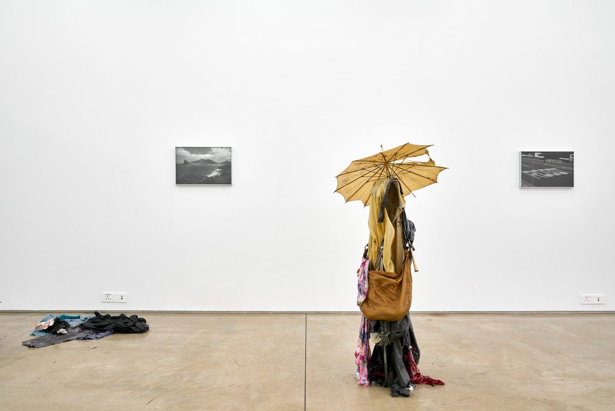 Installation photograph from the ‘without a clear discernible image’ exhibition in A4’s Gallery. On the left, Kevin Beasley’s untitled resin and garment sculpture sits on the floor, with Beasley’s monochrome photograph ‘Hout Bay’ mounted on the wall. On the right, Beasley’s untitled garment and resin sculpture stands on the floor, with Beasley’s monochrome photograph ‘Robot’ mounted on the wall.
