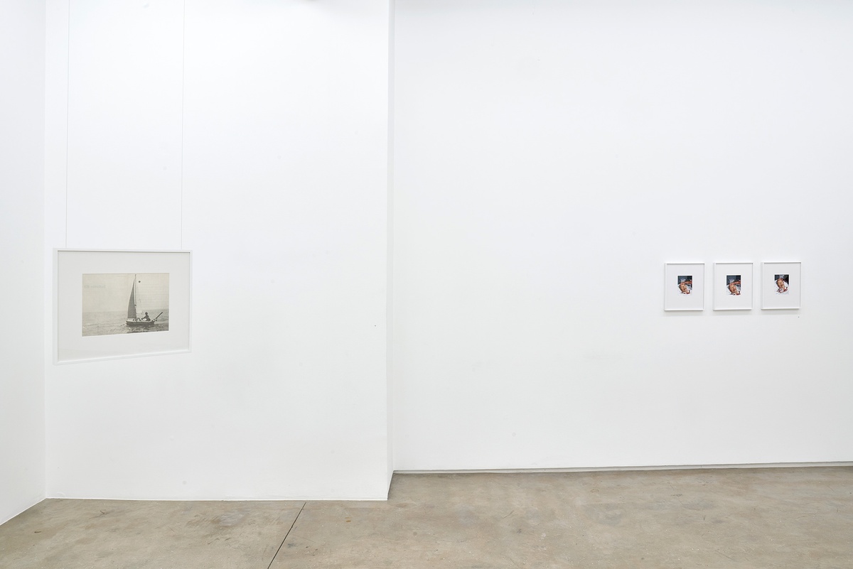 Installation photograph of the You to Me, Me to You exhibition. On the left, Bas Jan Ader’s framed ‘Bulletin 89, in search of the miraculous (songs for the north atlantic)’ is suspended from the ceiling. On the right, Pieter Hugo’s framed photographic triptych ‘944-03-03, MALE, MARRIED, 2021-12-21, CAPE TOWN, NATURAL CAUSES’ is mounted on a white wall.
