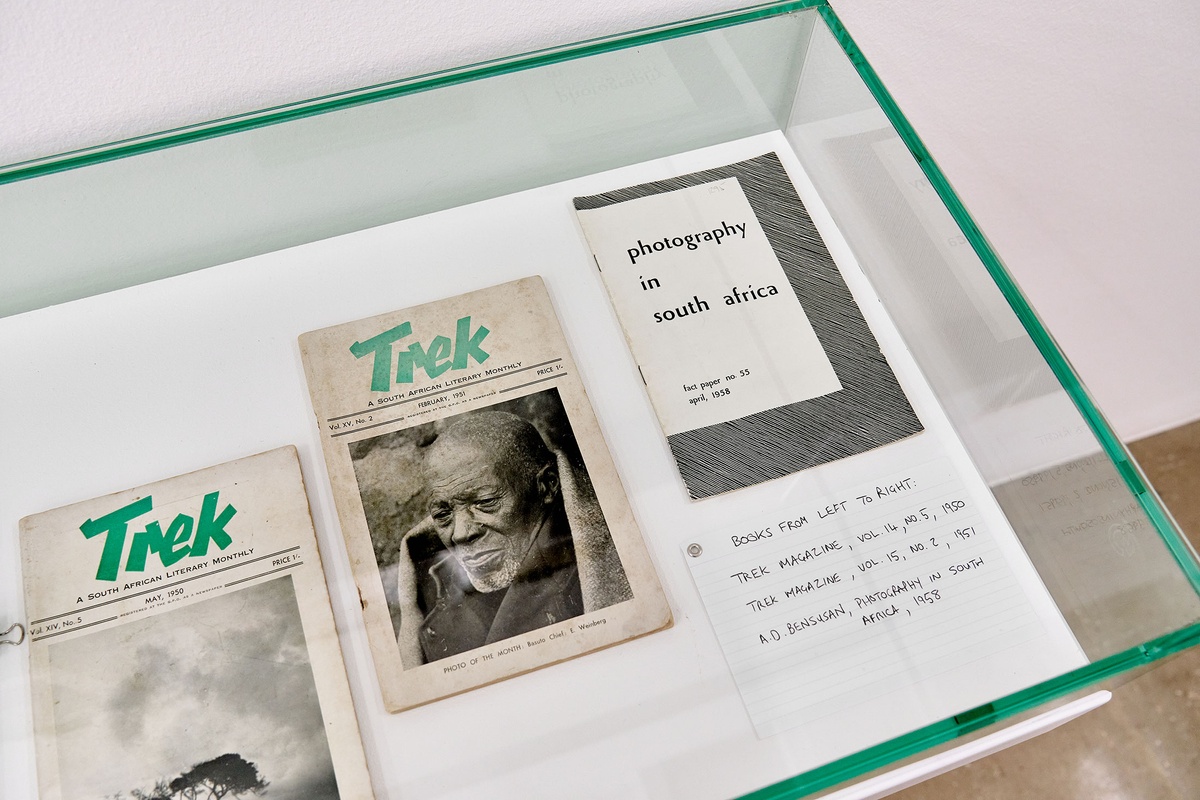 Installation photograph from the Photo Book! Photo-Book! Photobook! exhibition in A4’s Gallery. A glass display case holds two editions of ‘Trek: A South African Literary Monthly’ and one edition of the ‘Photography in South Africa’ fact paper.
