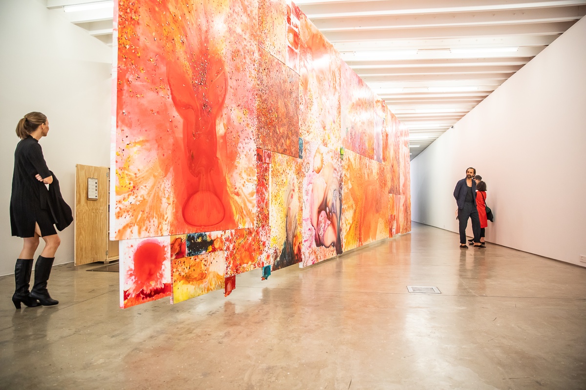 Event photograph from the preview of the 'A Little After This' exhibition in A4 Arts Foundation. In the middle, an installation of Penny Siopis' glue, ink and oil 'Maitland' paintings is suspended from the ceiling. On the left and right, attendees examine the installation.
