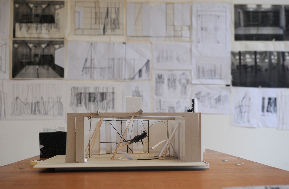Process photograph from Unathi Mkonto’s residency on A4’s top floor. At the front, a small paper exhibition mockup sits on a wooden table. At the back, process drawings line the wall.
