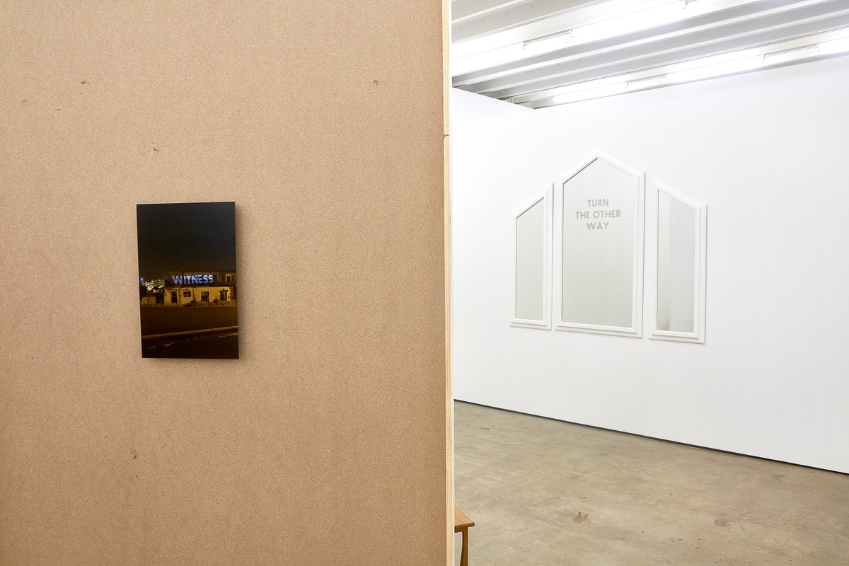 Installation photograph from the 2018 rendition of ‘Parallel Play’ in A4’s Gallery. On the left, Haroon Gunn-Salie’s photograph ‘Witness - a site-specific intervention’ is mounted on a freestanding hardboard wall. On the right, Gunn-Salie’s mirror work ‘Turn the other way’ is mounted on the gallery wall.
