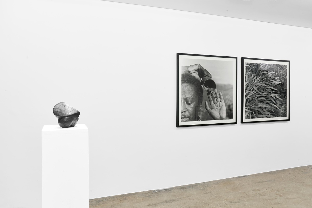 Installation photograph from the Customs exhibition in A4’s Gallery. On the left, Ezrom Legae’s bronze sculpture ‘Face’ sits on a white plinth. On the right, George Hallett’s framed monochrome photographic diptych ‘Peter Clarke’s Tongue’ is mounted on a white gallery wall.
