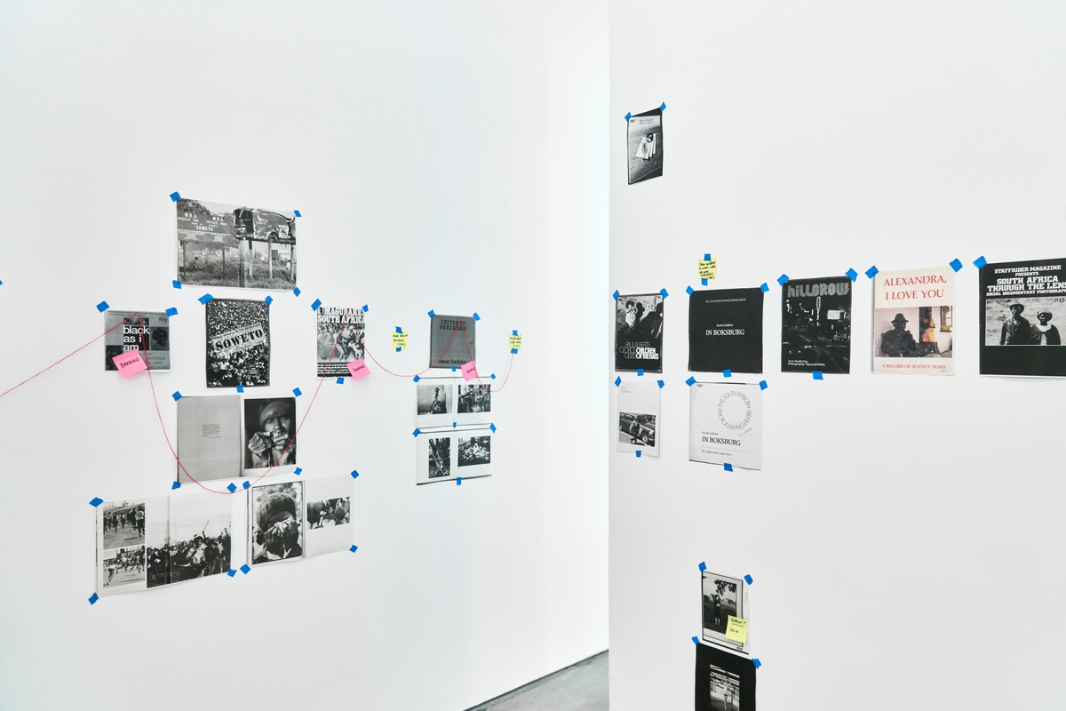 An installation photograph from ‘Photobooks’, Sean O’Toole’s Course of Enquiry at A4. Photocopies from various photobooks are taped to the walls on the left and right, with selected copies connected by read thread.
