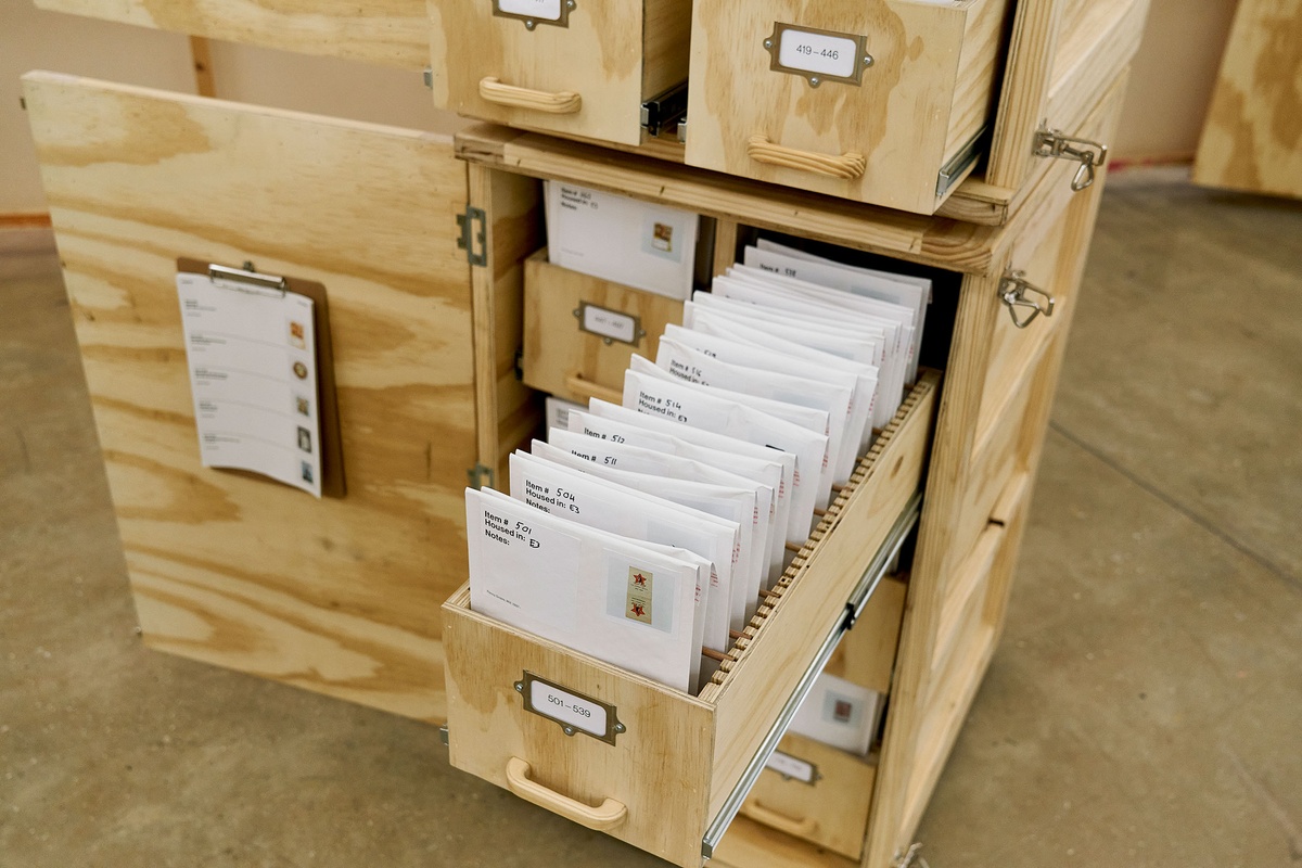 Installation photograph from the 'A Little After This' exhibition in A4 Arts Foundation's gallery that shows collected objects from Penny Siopis' 'Will' work organised in envelopes, which in turn are arranged in bespoke wooden filing cabinets.
