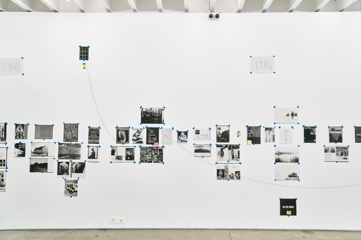 An installation photograph from ‘Photobooks’, Sean O’Toole’s Course of Enquiry at A4. Photocopies from various photobooks are taped to the wall under the heading ‘1970’s’ with a red thread connecting selected copies.
