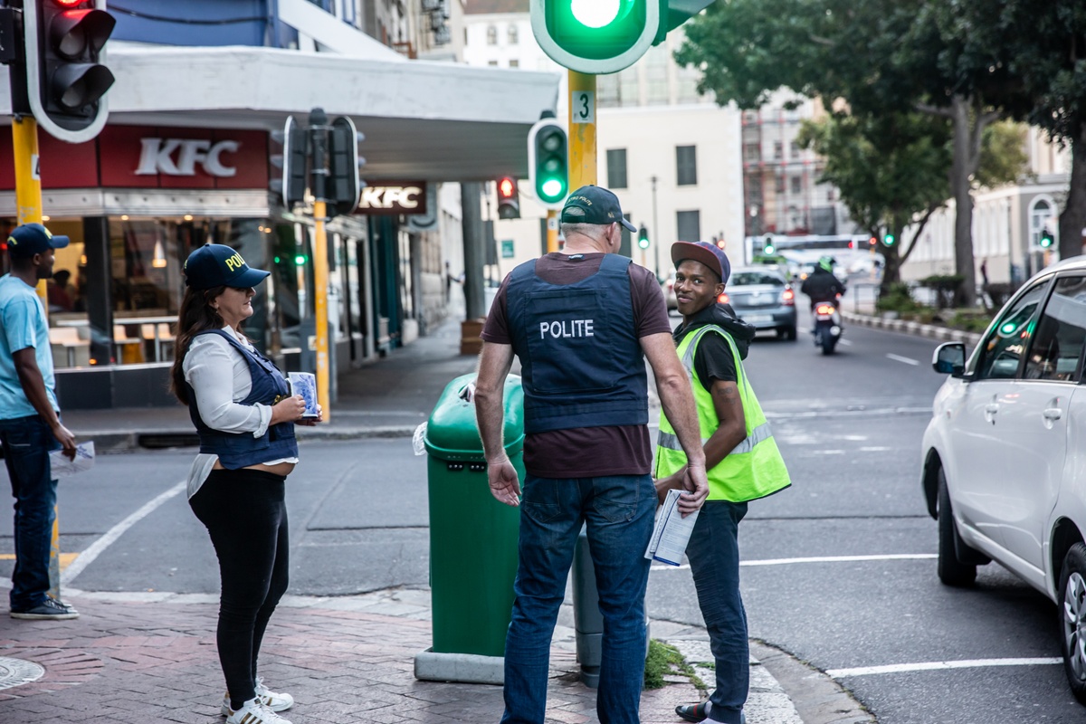 Process photograph from the 2019 rendition of Christian Nerf’s performance piece ‘Polite Force’. Two participants wearing ‘Polite Force’ riot gear interact with a member of the public on a street corner.
