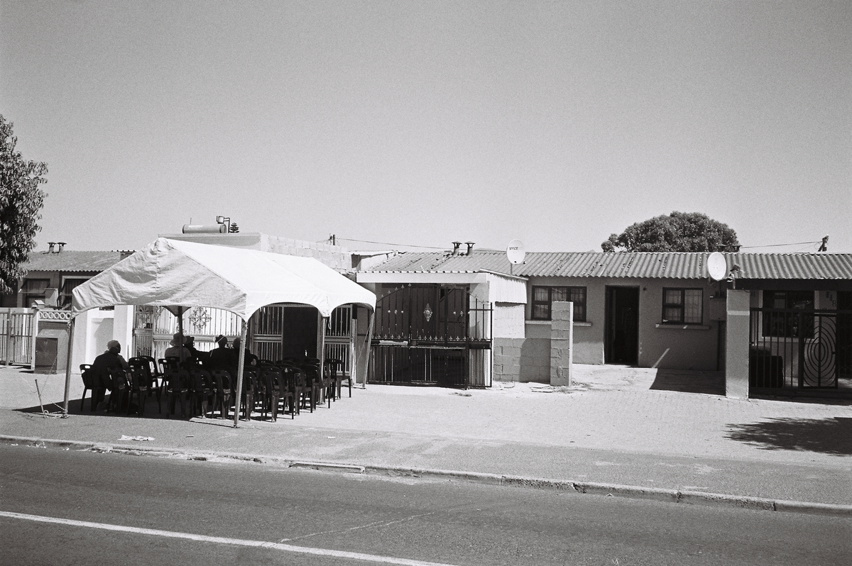 A photography from the Gladys' House workshop coordinated by Kemang Wa Lehulere in NY1, Guguletu shows a marquee with chairs set up on the pavement in front of a house.
