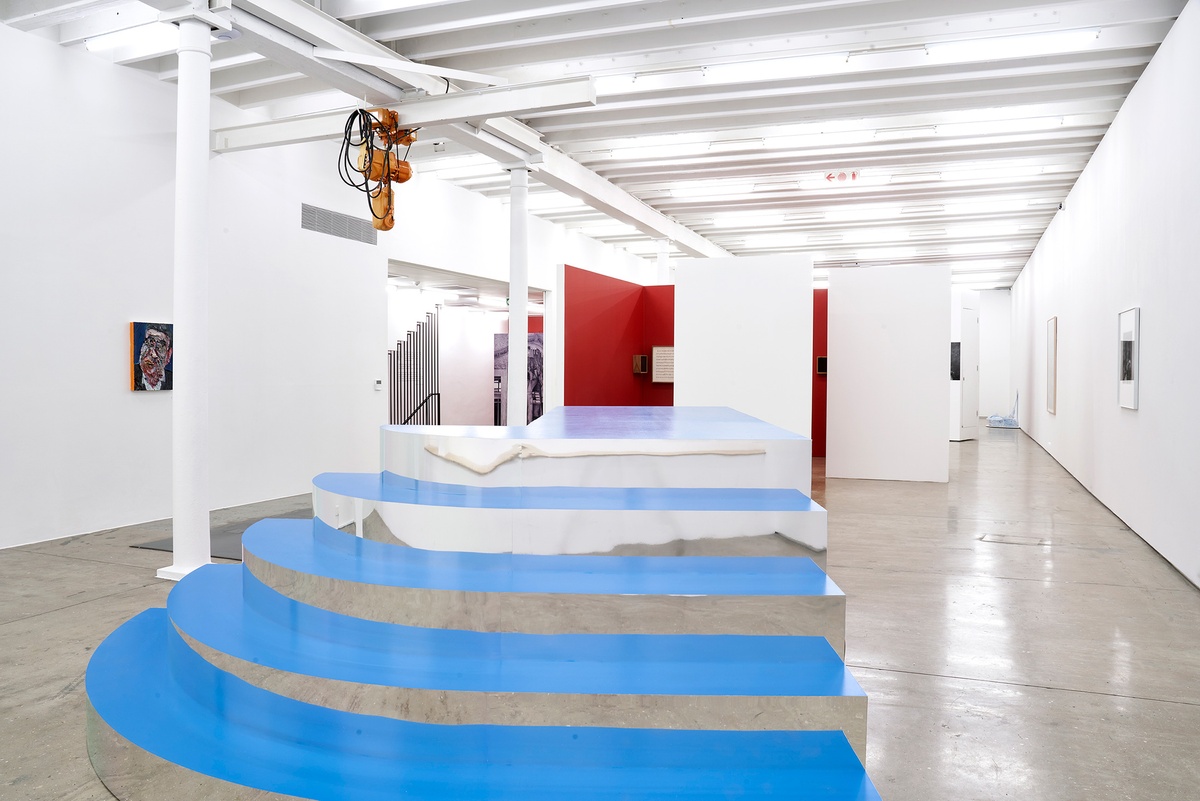 Installation photograph of the You to Me, Me to You exhibition. At the front, Slavs and Tatars’ installation ‘To No One and to Two’ consists of a platform with aluminium inlays at the back of the steps on the gallery floor. On the left, Georgina Gratrix’s oil painting ‘The Insomniac’ is mounted on a white gallery wall. At the back, four of Iñaki Bonillas’ sound and score installations from ‘The Return to the Origin’ series are mounted on freestanding walls painted white on the outside and red on the inside.
