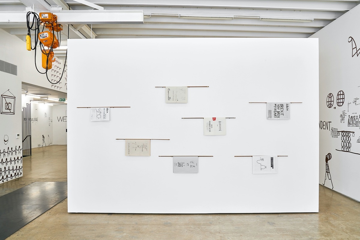Installation photograph from Dan Perjovschi’s ‘The Black and White Cape Town Report’ exhibition in A4’s Gallery. A moveable gallery wall features a series of printed booklets attached to wooden dowels along the spine.
