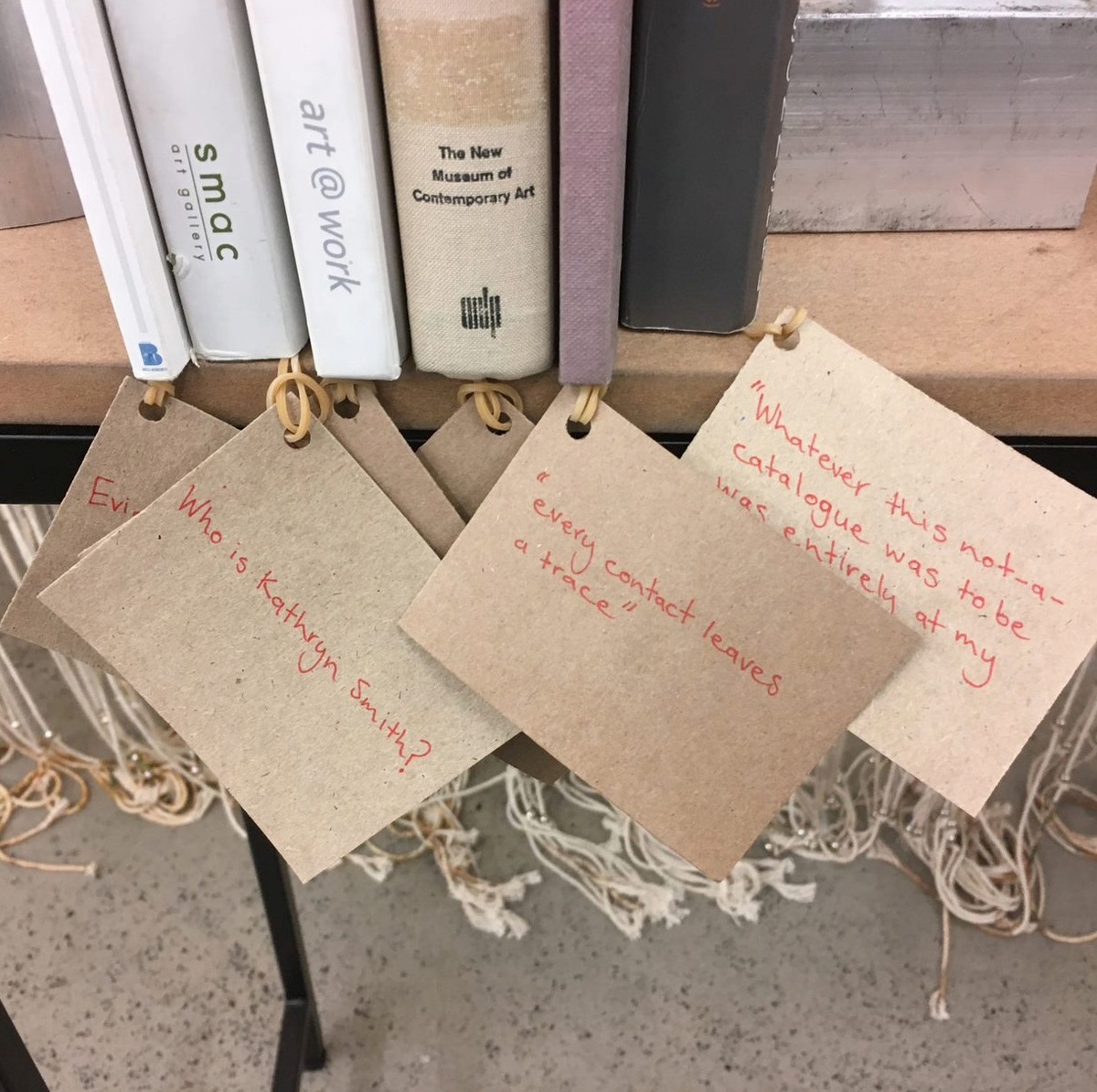 Process photograph from Kathryn Smith’s 2019 residency on A4’s top floor. A small collection of books pertaining to Smith’s practice sit on the edge of a table, each with a brown cardboard tag attached to it. One card reads “every contact leaves a trace” in red ink.
