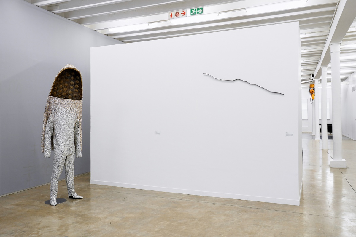 Installation photograph from the ‘Sounding the Void, Imaging the Orchestra V.1’ exhibition in A4’s Gallery. At the left, Nick Cave’s sculpture ‘Soundsuit’ stands on the gallery floor. On the right, Kyle Borland’s mild steel sculptural object ‘Ruler’ is mounted on a moveable gallery wall.
