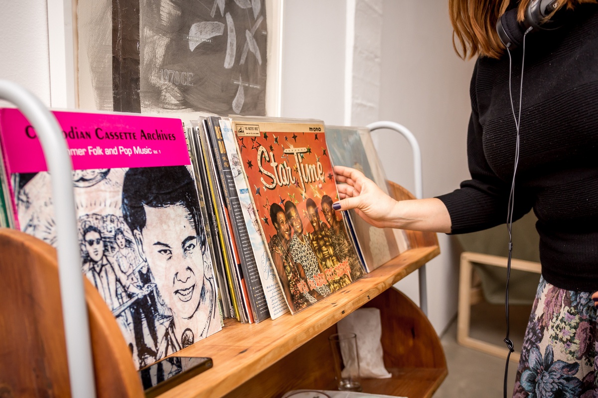 Event photograph from the opening of the You & I exhibition in A4’s Gallery. On the left, a bookshelf holds a selection of vinyl records. On the right, an attendee wearing a pair of headphones.

