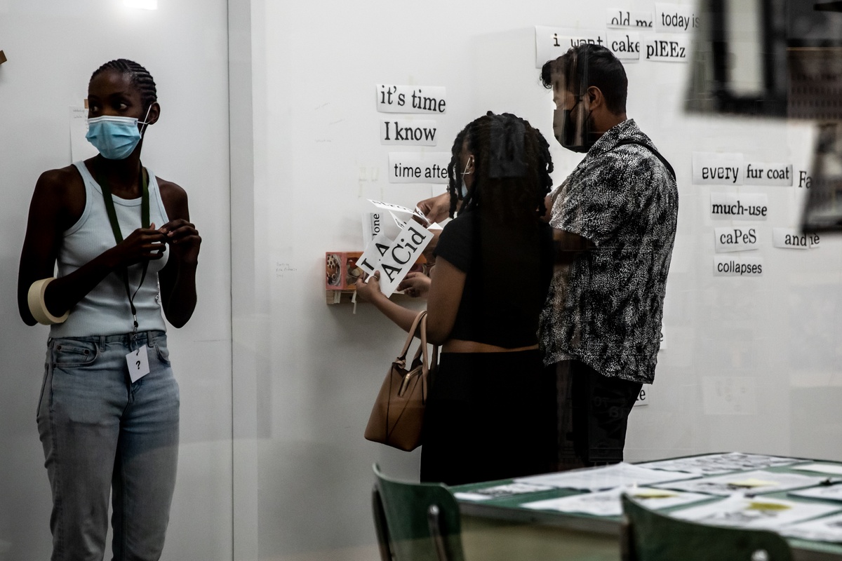 Event photograph from the opening of the Papertrails exhibition in A4’s Reading Room shows two participants combing through printed word fragments to stick onto the wall.
