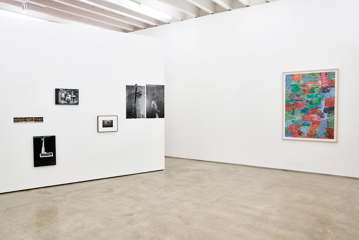 Installation photograph of the You to Me, Me to You exhibition. On the left, Thembinkosi Hlatshwayo's photographic installation with photographs mounted on a white movable gallery wall. On the right, Moshekwa Langa's mixed media on paper artwork 'Index Drawing (you give me the creeps)' is framed and mounted on a white gallery wall.
