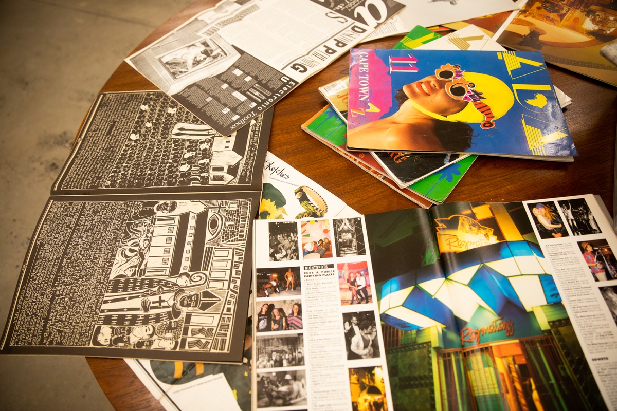 Event photograph from the opening of the Papertrails exhibition in A4’s Reading Room shows printed matter strewn on a round wooden table.
