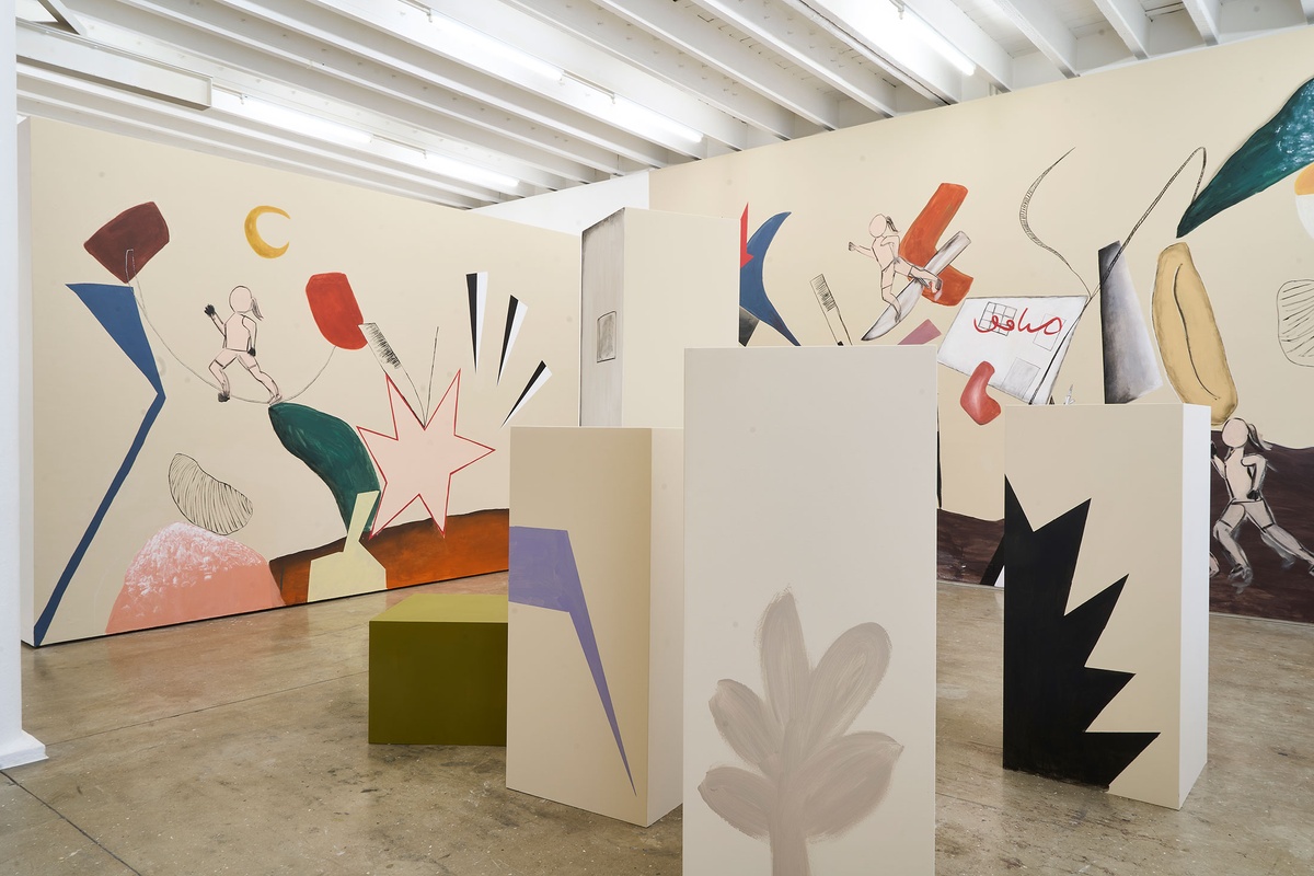 Installation photograph of Common exhibition, featuring an installation by Hanna Noor Mahomed called ‘The Prodigal Daughter.’ On the right, a group of plinths painted with geometrical shapes and objects to resemble a city. At the back, a wall mural with four femme figures running among various objects and geometrical shapes.
