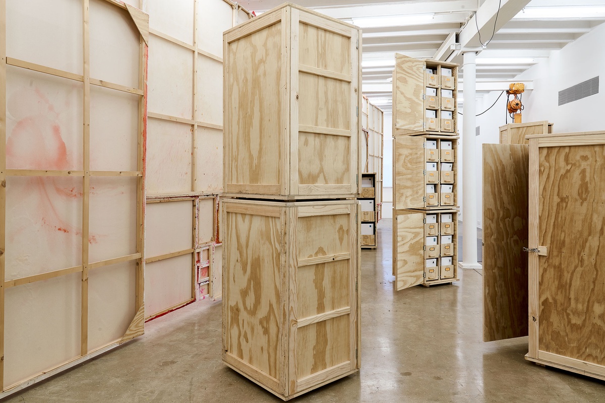 Installation photograph from the 'A Little After This' exhibition in A4 Arts Foundation's gallery. In the middle, collected objects from Penny Siopis' 'Will' work are stored in envelopes and wooden crates. On the left, the back of an installation of Penny Siopis' glue, ink and oil 'Maitland' paintings suspended from the ceiling.
