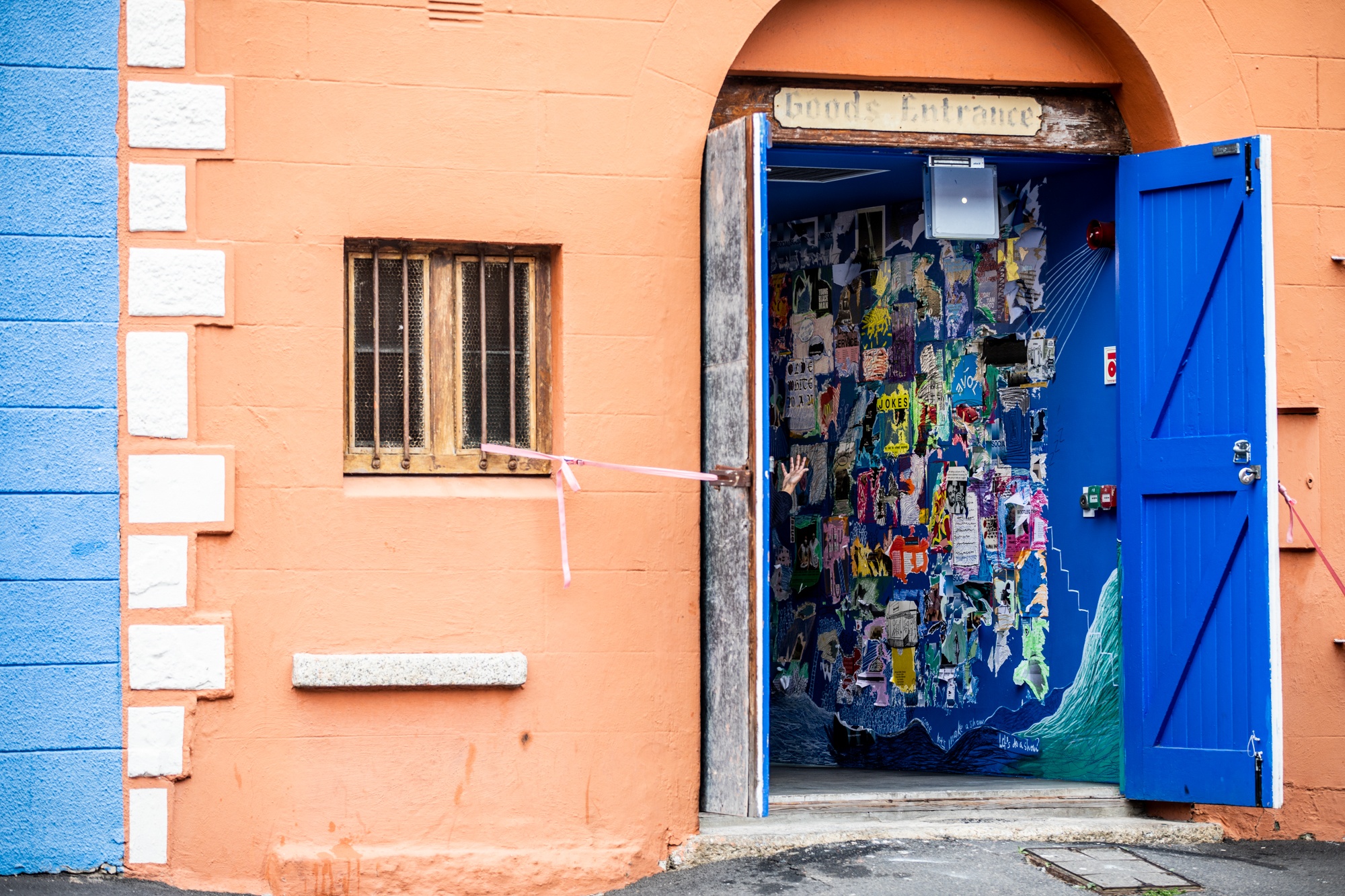 Event photograph from the opening of ‘Disruption’, Hanna Noor Mahomed’s residency in A4’s Goods project space. From the Goods entrance, a collage of poster fragments and drawing interventions are visible on the wall.
