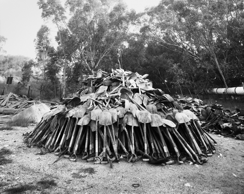 David Goldblatt's monochrome photograph's monochrome photograph '“Lashing” shovels retrieved from underground. Every grain of sand in the yellow tailings dumps that made the Witwatersrand landscape and every grain of gold that made its wealth, came from a rock off a black man’s shovel underground. Central Salvage Yard, Randfontein Estates, Randfontein, 1966' shows a heap of shovels.

